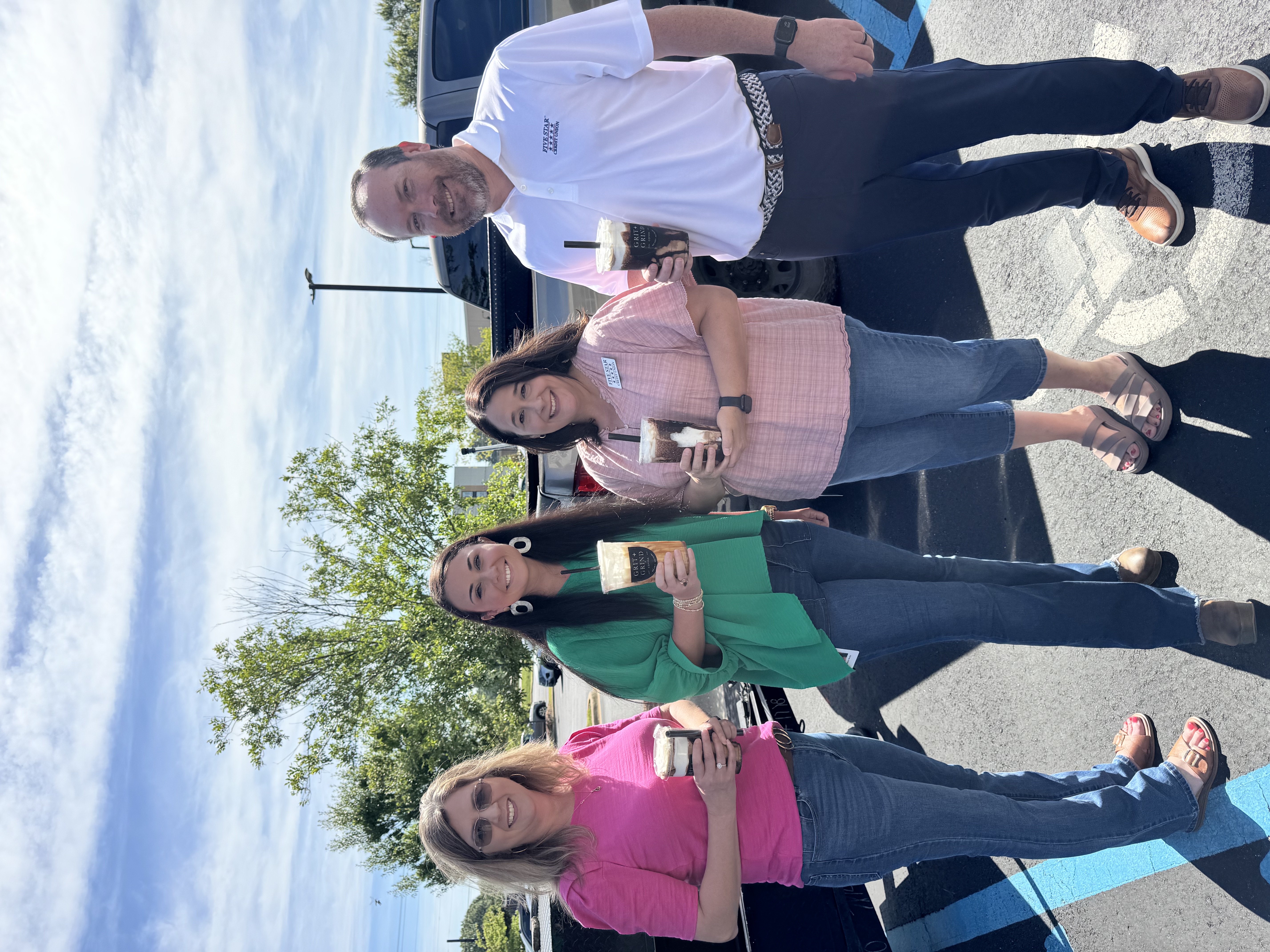 Four employees smiling while holding iced coffee drinks