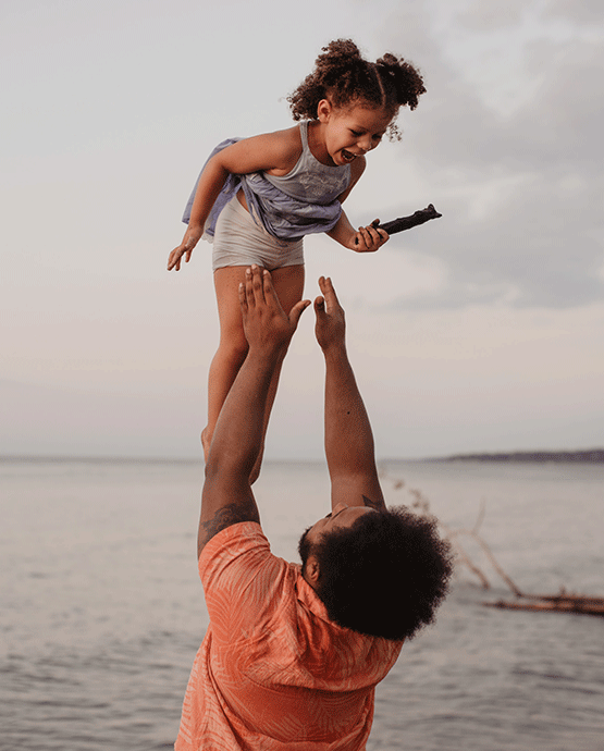 Dad throws his daughter in the air at the beach. 